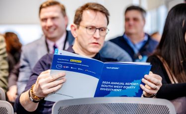 A man in an audience reading a report called The 2024 Annual Report: South West Investment